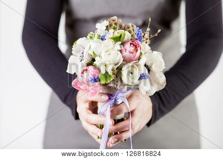 Woman in grey dress and black shirt is giving spring bouquet from pink tulips violet grape hyacinths white anemones violet veronica and white buttercup with violet ribbon