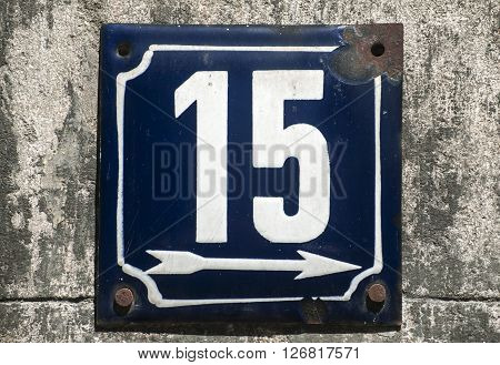 Weathered grunge square metal enameled plate of number of street address with number 15 closeup