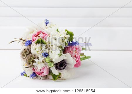 Bouquet from pink tulips violet grape hyacinths white anemones violet veronica and white buttercup with violet ribbon lying on the floor with white wooden shutter background