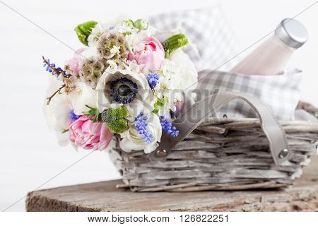 Bouquet from pink tulips violet grape hyacinths white anemones violet veronica and white buttercup with violet ribbon lying in the picnic basket with milkshake in the bottle and sweets in the jar with white background and the old wooden bench
