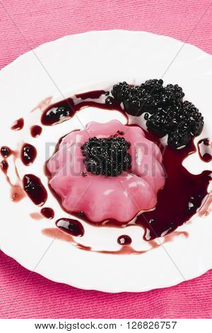 Pudding with sauce of brambleberry is on white plate on pink background.