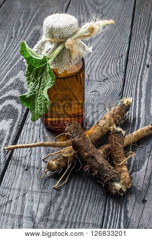 Medicinal plant - a burdock. The roots and leaves of burdock burdock oil in bottle on a wooden background. It is used for the treatment and care of hair
