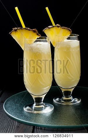 Refreshing pineapple cocktail with coconut cream in glasses with slices of pineapple and cocktail straws on a glass tray