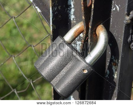 Old rusty padlock on metal mesh-netting fence with door with flaked paint