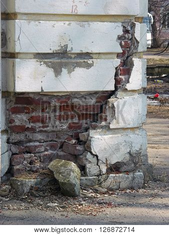 Old dilapidated stucco corner of building with red bricks in deep fissure