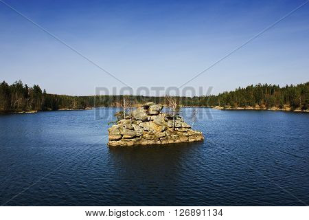 Forest landscape: stone island in the middle of the lake with trees growing on it on a sunny day. Ottenstein lake in Lower Austria.