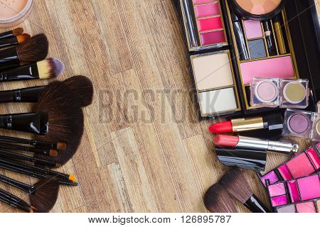set of brushes, lipsticks, maskara, eye shadows and  powder on wood borders, top view with copy space