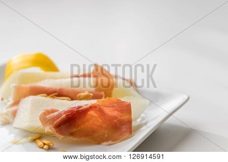 Detail of prosciutto slices with water melon. Peel and seeds. Starter in soft focus on white plate. Neutral background.