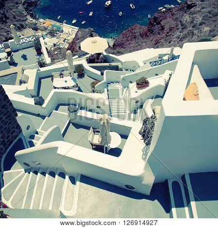 grey and white staircases leading down to beautiful Amoudi bay in volcanic village Oia, Santorini, Greece. square vintage toned image