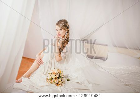 Beautiful bride in white dress on the bed in her bedroom