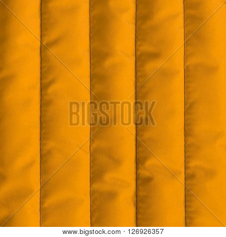 Orange quilted textiles with insulation texture. Vertical stripes. Close up fragment of the top view.