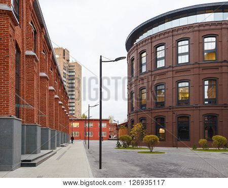 Extensive office complex exterior in loft style. Red brick buildings of former factory gasholders. Evening artitecture lighting street lamps.