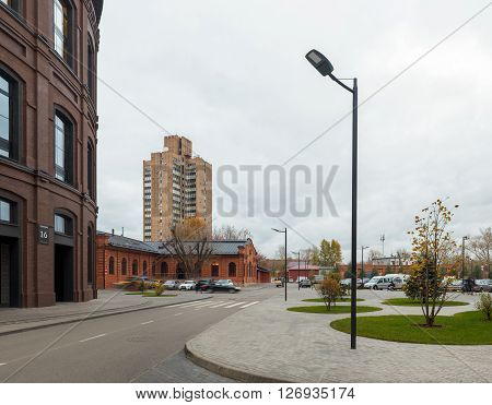 Extensive office complex exterior in loft style. Red brick buildings of former factory gasholders. Evening architectural lighting street lamps.