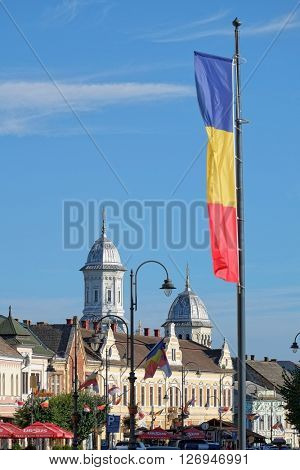 TURDA, ROMANIA - AUGUST 09, 2015: the Romanian flag waving on skyline of downtown Turda in Transylvania