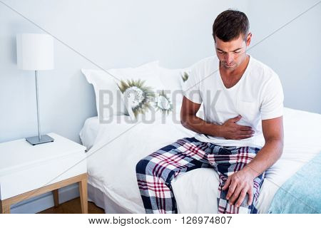 Young man sitting with stomach pain on bed in bedroom