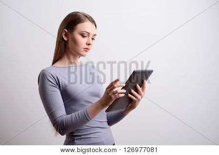 Always connected. Pleasant concentrated magnetic woman holding tablet and using it while standing  isolated in grey background