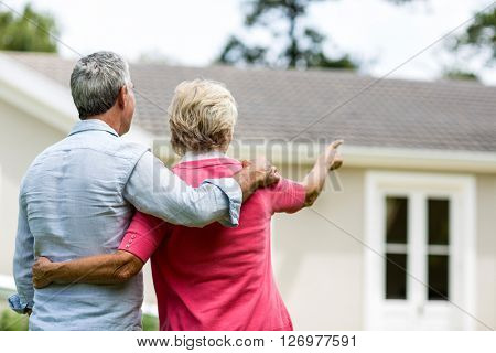 Rear view of senior couple looking at house while standing ih yard