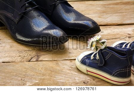 fathers day small blue kids sneakers with a bouquet of daisies standing in front of daddy's black shoes on rustic wooden planks