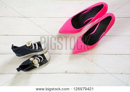 mother's day kids sneakers with a bouquet of daisies and mum's pink highheel stilettos on white wood view from above copy space