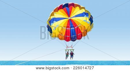 Happy Couple Parasailing On Tropical Beach In Summer. Couple Under Parachute Hanging Mid Air. Having