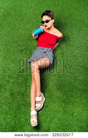 Overhead View Of Beautiful Woman With Beverage In Paper Cup Resting On Green Lawn