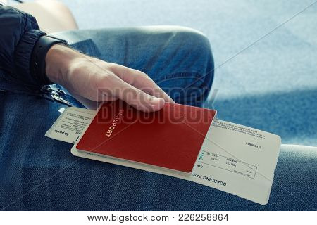 Man In Blue Jeans Sits And Holds In His Hand Passport Of Red Color With Tickets To Plane. Сlose Up. 