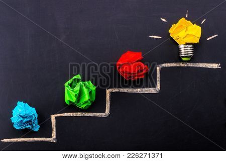 Evolving Idea Concept With Colorful Crumpled Paper And Light Bulb On Steps Drawn On Blackboard.