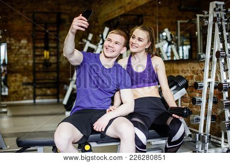 Beautiful Happy Couple In Sports Clothes Is Making Selfie Using A Smart Phone And Smiling While Rest