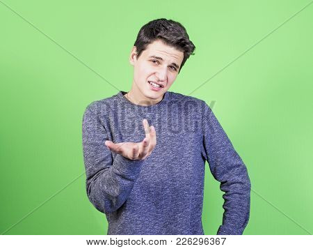 A Puzzled Young Man Reproaches Someone, Wears A Casual Sweater, Isolated On A Light Background. The 