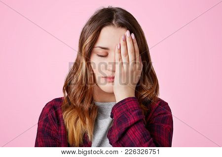 Isolated Shot Of Pretty Frustrated Overworked Female Covers Face With Hand, Keeps Eyes Shut, Being S