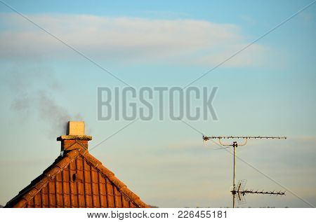 Smoke Out Of A Chimney On Top Of A Roof With A Radio Mast Next To It.