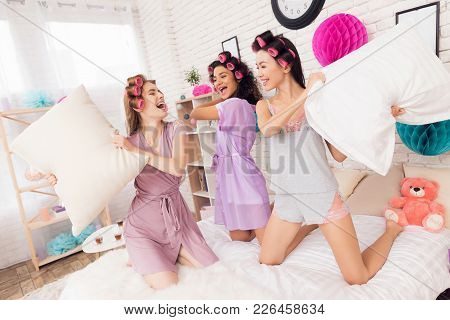 Three Girls With Curlers In Their Hair Pillowfight. They Are Celebrating Women's Day March 8.