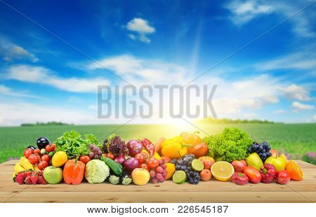 Vegetables and fruit on wooden table of boards against background of spring field and bright blue sky.