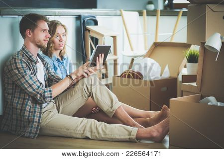 Young couple moving in new home.Sitting and relaxing after unpacking.Looking something on laptop. Young couple