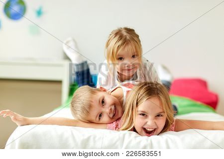 childhood, leisure and family concept - happy little kids having fun in bed at home