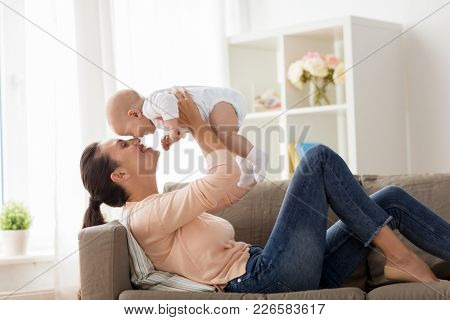 family, motherhood and people concept - happy mother with little baby boy lying on sofa at home