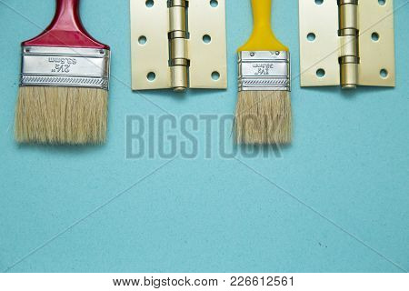 Home, House Repair, Redecorating, Renovating Concept. A Door Hinges And Two Brushes On A Blue Backgr
