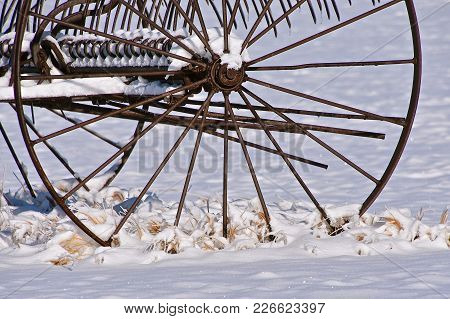 The Steel Wheel Of An Old Dump Rake Left In The Snow