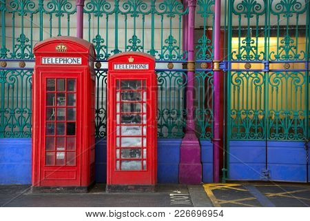 Two red booths in two different sizes with green and blue iron fence in background in Smithfield market in London UK