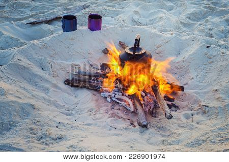 Cooking Coffee While Traveling On The Wild Seashore - Two Mugs Stand Next To Bonfire With Small Kett