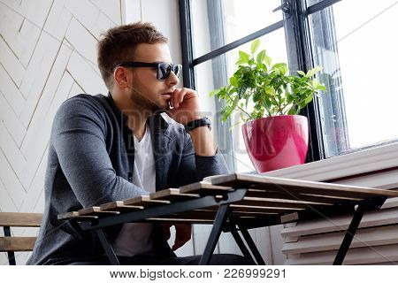 Casual Man In Sunglasses Sitting At The Table Near Window.