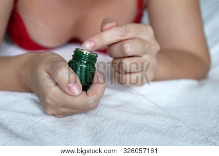 Woman In Lingerie Applies Green Herbal Balm From The Bottle To The Skin Lying On The Bed. Concept Of