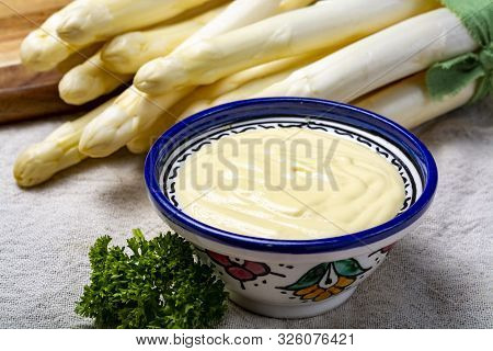 Bunch Of Fresh Uncooked White Asparagus And Hollandaise Sauce In Bowl