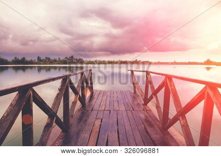 Old Wooden Pier Bridge Leading To The Lake With Beautiful View And Skyscape At The Sunset.