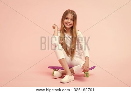 Enjoying Vibes On Penny Board. Cute Little Child Sitting On Penny Board Deck On Pink Background. Ado
