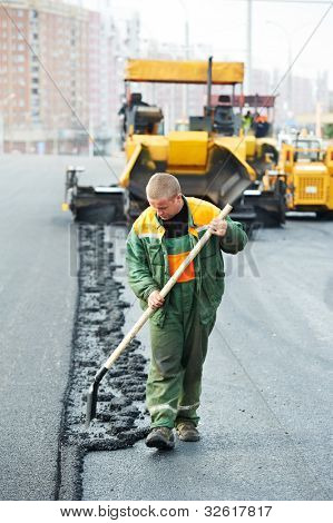 Trabajador con pala delante de la máquina pavimentadora de asfalto durante la construcción de carreteras y obras de reparación