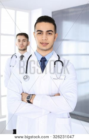 Arab Doctor Man Standing With Caucasian Colleague In Medical Office Or Clinic. Diverse Doctors Team,