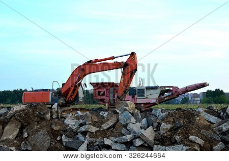 Heavy Excavator Working At Construction Site. Unloading Old Stone Or Concrete Waste Into A Mobile Ch