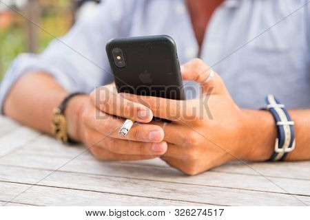 Knokke/belgium-09.08.19 : Man Holding A Cigarette Smoking While Using His Smartphone Iphone Apple