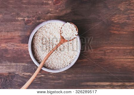 A Bowl Of Uncooked Rice On The Wooden Table, Top View.